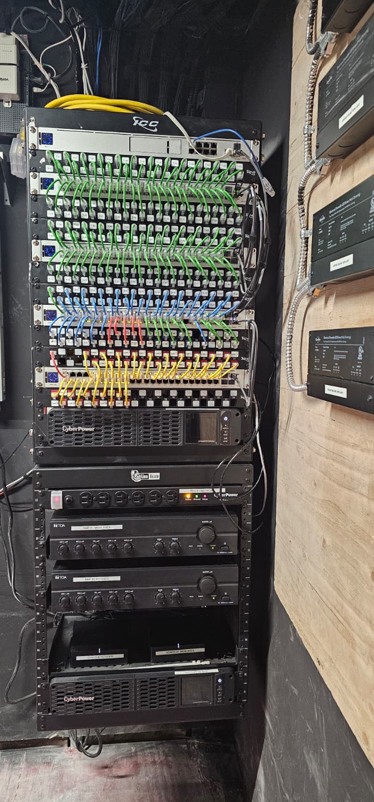 Finished rack with color-coded patch cabling, managed switches, zoned audio amplifiers, and dual UPS units